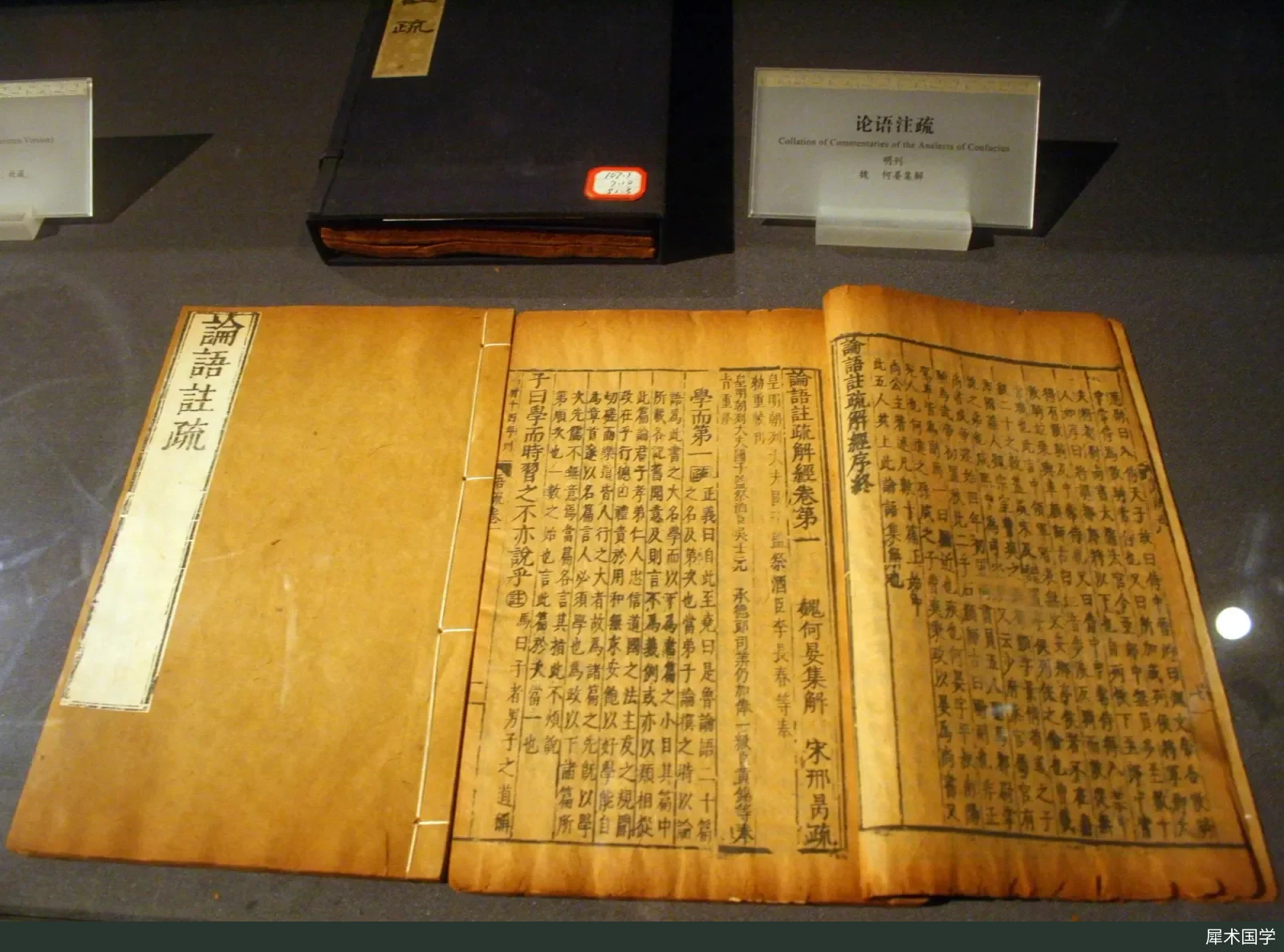 A Ming-dynasty printed edition of He Yan's Collected Explanations of the Analects on display at the Shandong Museum: an open thread-bound book shows vertical woodblock-printed text, with the classic in large characters and the commentary in small characters